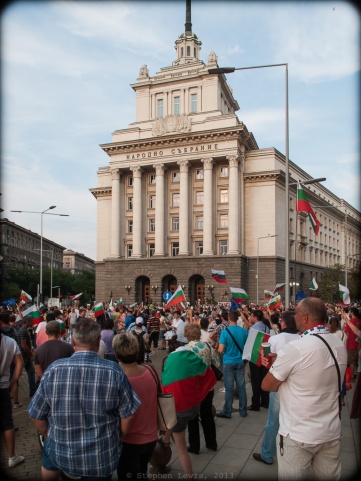 Sofia, Bulgaria.  Demonstrators gathering on a recent weekday evening in front of the National Assembly Building, a "Stalinist Wedding Cake" style edifice that during the years of the Soviet Bloc housed the headquarters of the Bulgarian Communist Party.  Out of frame to the left: The offices the Bulgarian Council of Ministers.  Out of frame to the right: The offices of the President of the Republic of Bulgaria. The National Assembly Building, by the way, stands at the very epicenter of Sofia, at the convergence of three ages-old roadways around which the city rose, at the remains of the east gate of the Roman city of Serdica, and at the foot of a rise upon which, during Ottoman times, stood the clock tower that regulated the city's pace.  (Canon G10) (Click to enlarge.)