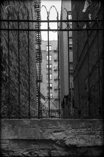 Courtyard, near Anderson Ave., West Bronx, 2012.  Note the traditional New York City fire escapes and the razor wire atop the original wrought iron fencing. (Fuji X100) Click to enlarge.